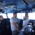 Zé and João to the right discussing the reactive approach to targeting multiple Mola positions on the NRP Argos. A crew member looks on.